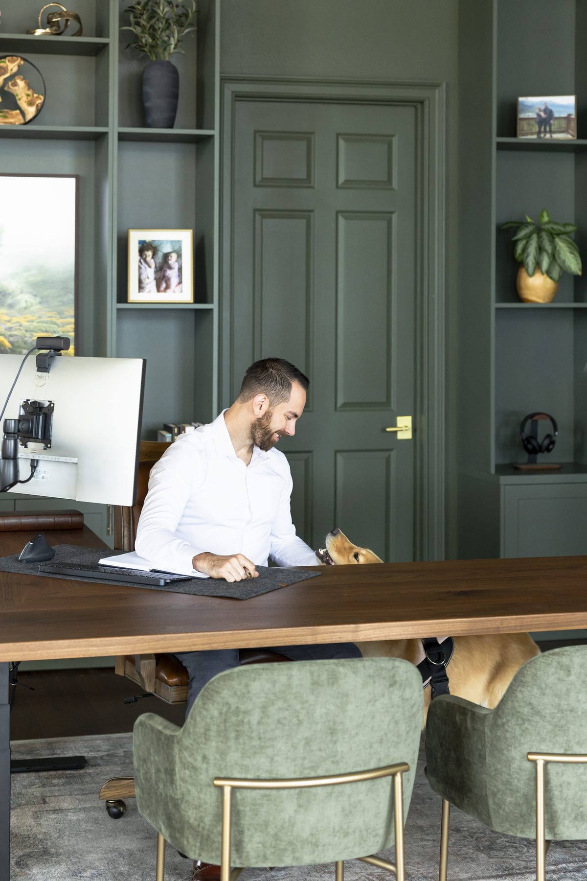 Jesse Plunkett at his desk in a white shirt, smiling down at his dog Nala