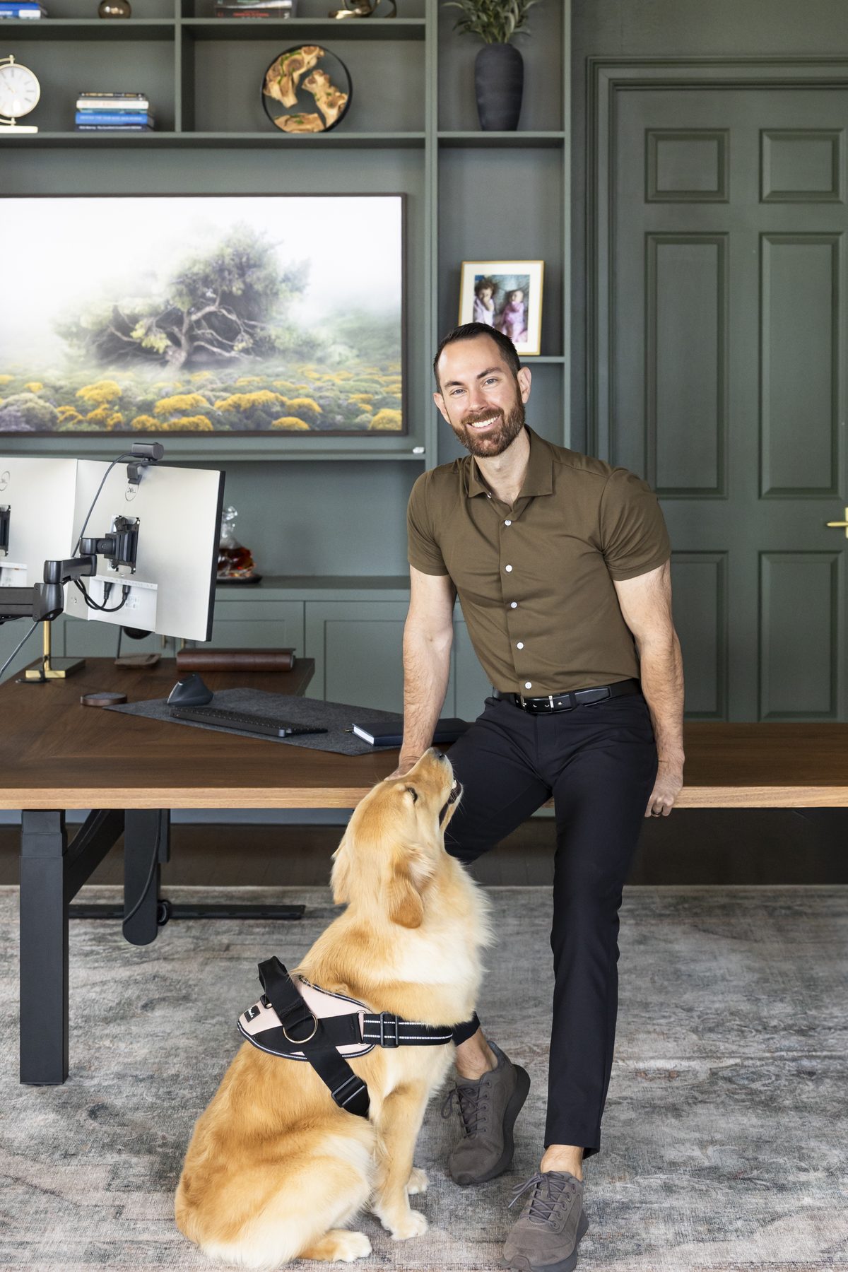 Jesse Plunkett seated on the edge of his desk while his golden retriever, Nala, looks up at him