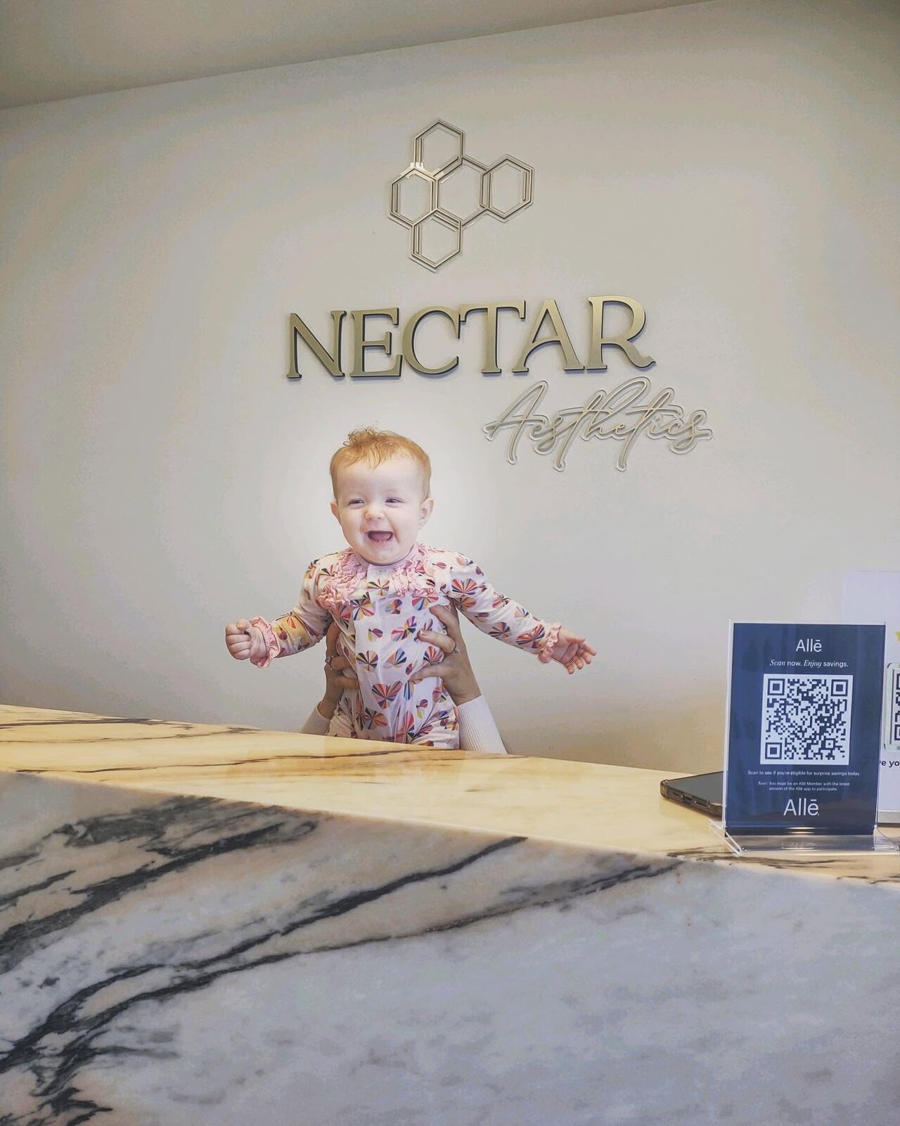 A laughing baby held up at the med spa's front desk