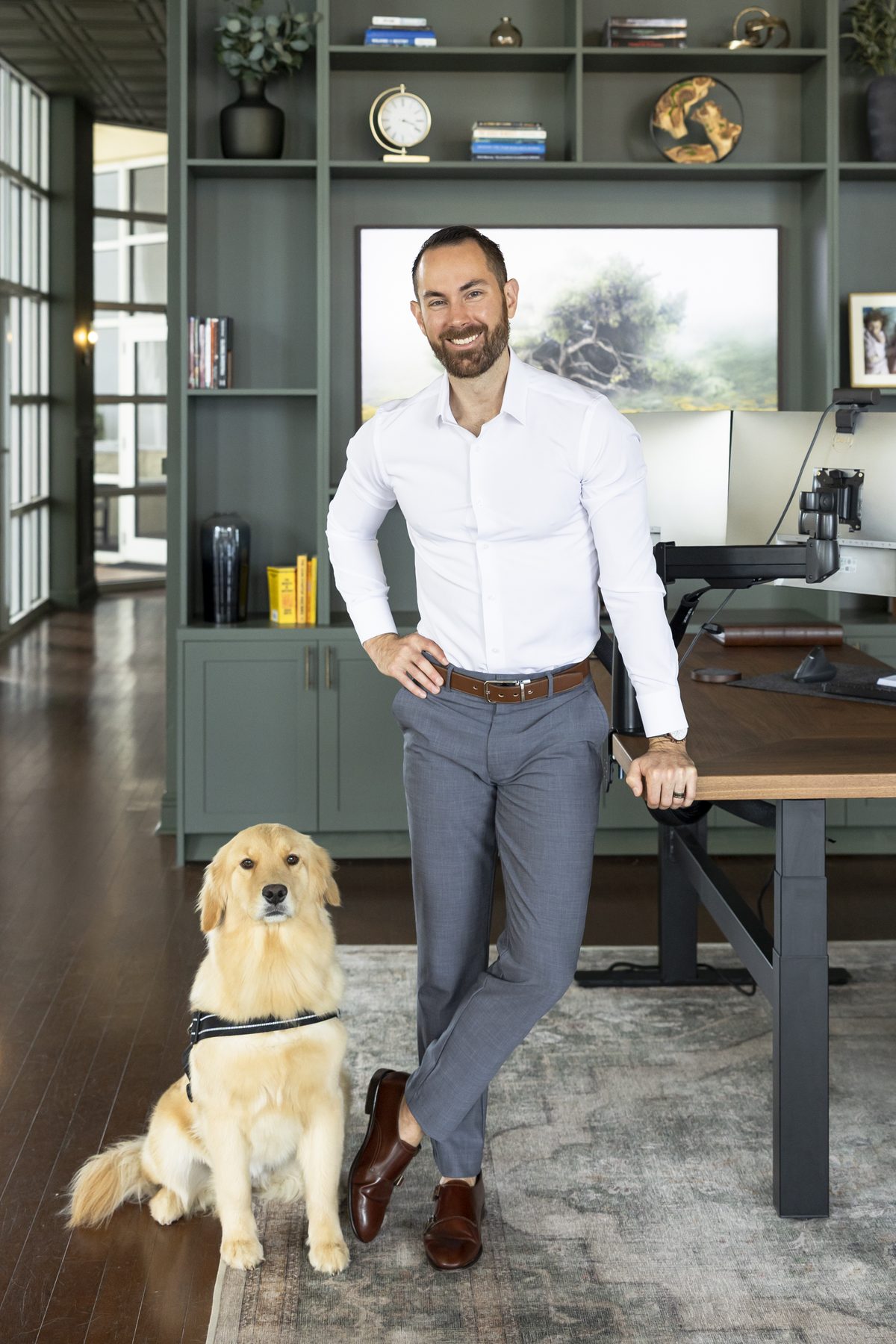 Jesse Plunkett leaning on his standing desk with his golden retriever, Nala, sitting at his feet